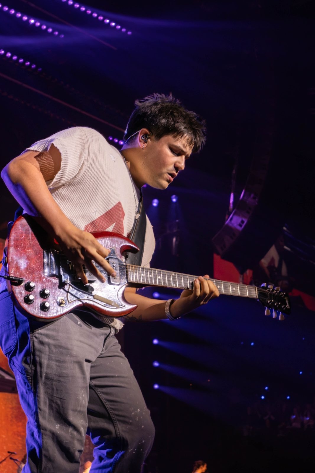 Guitarist bent over a red electric guitar in purple light