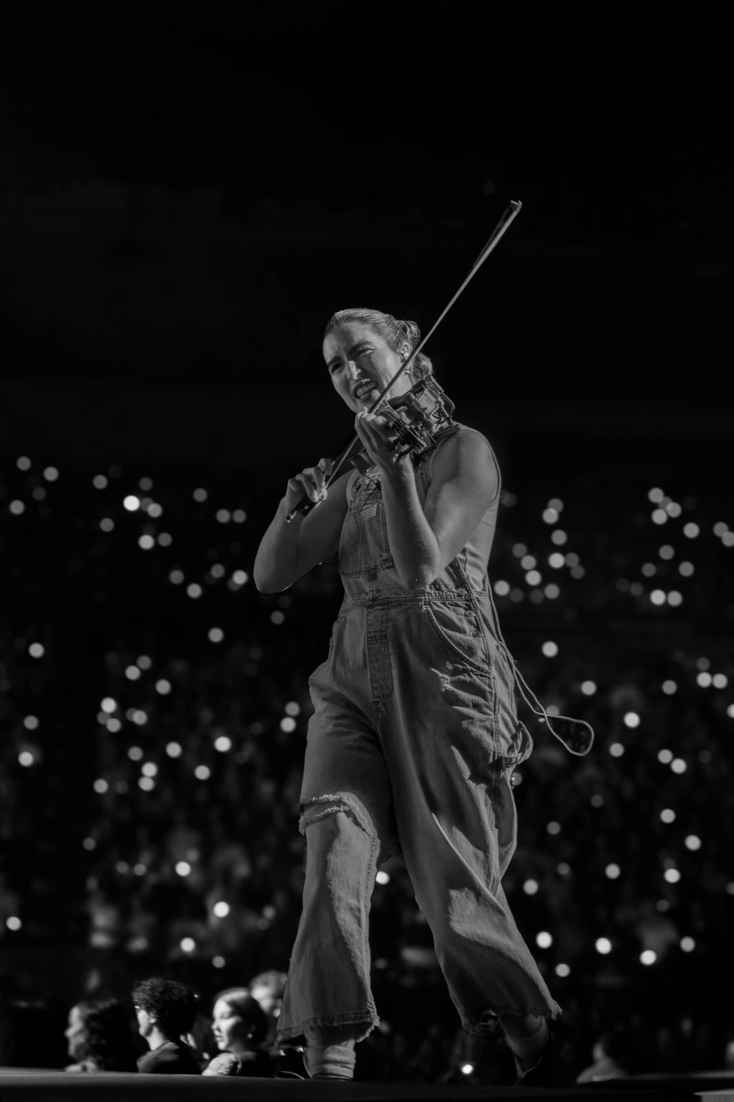 Black and white: violinist playing, phone lights in the crowd