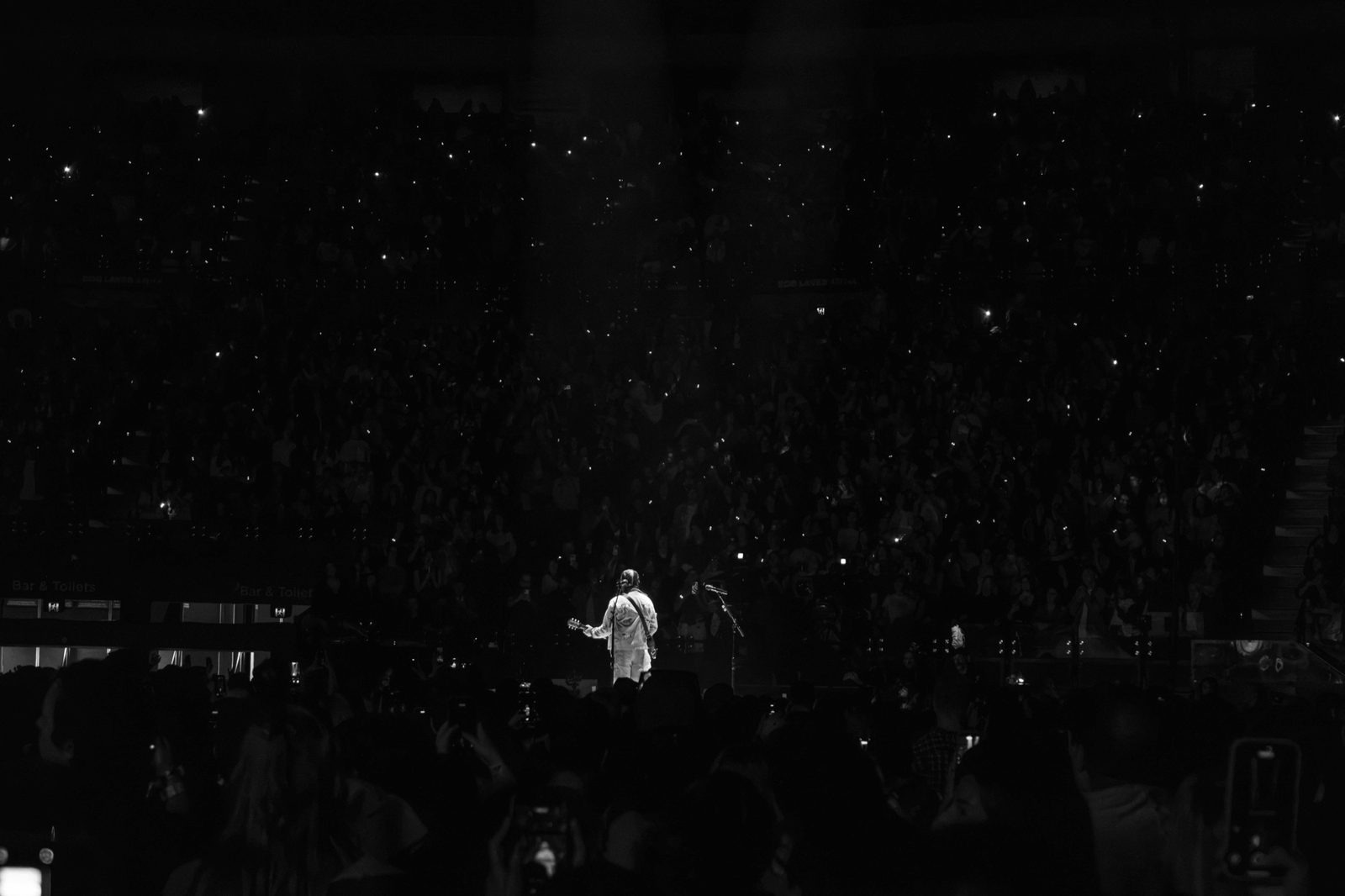 Black and white: a lone figure on a dark stage, crowd lights scattered