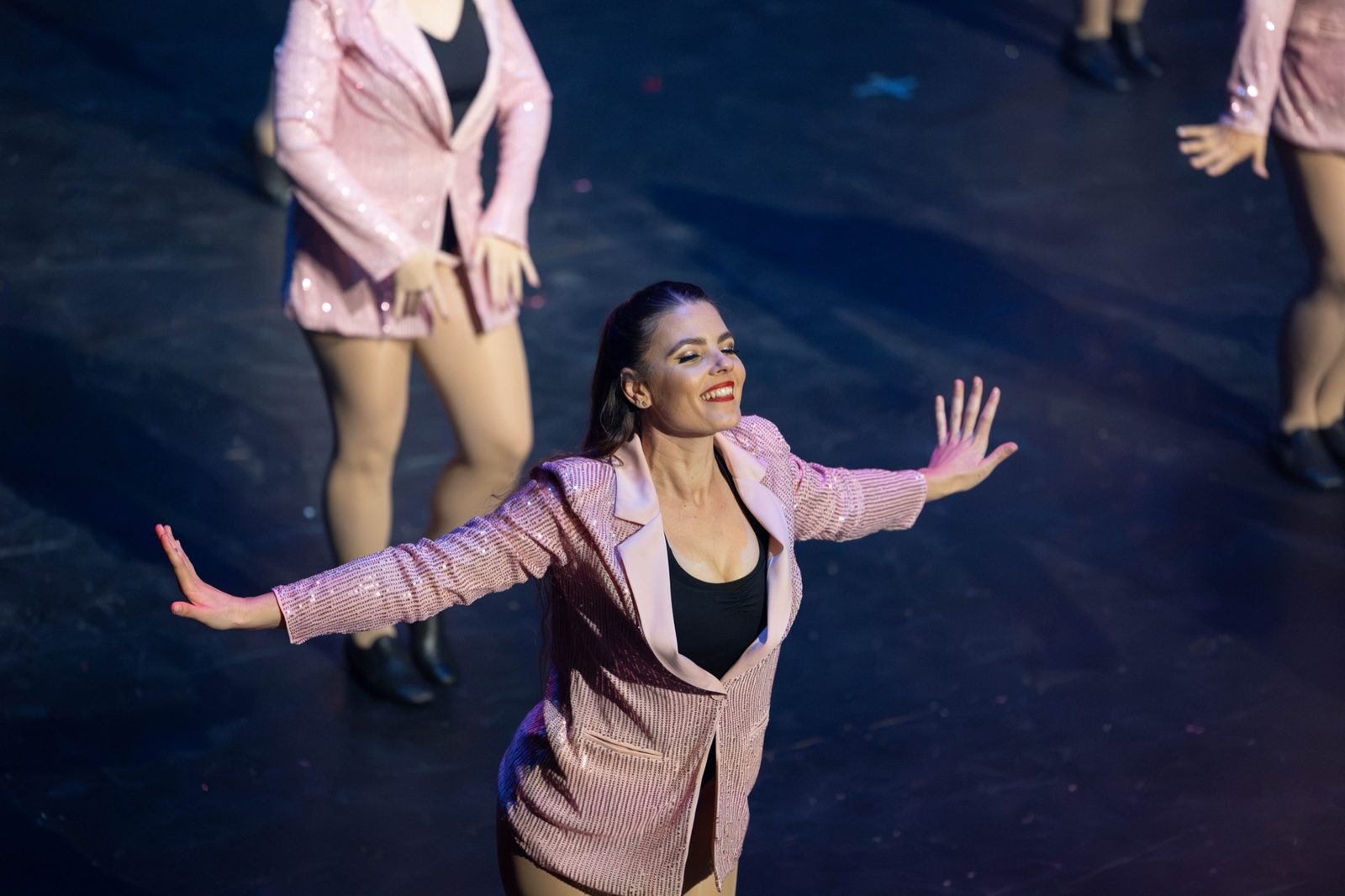 Dancer in a pink suit, arms flung wide on stage