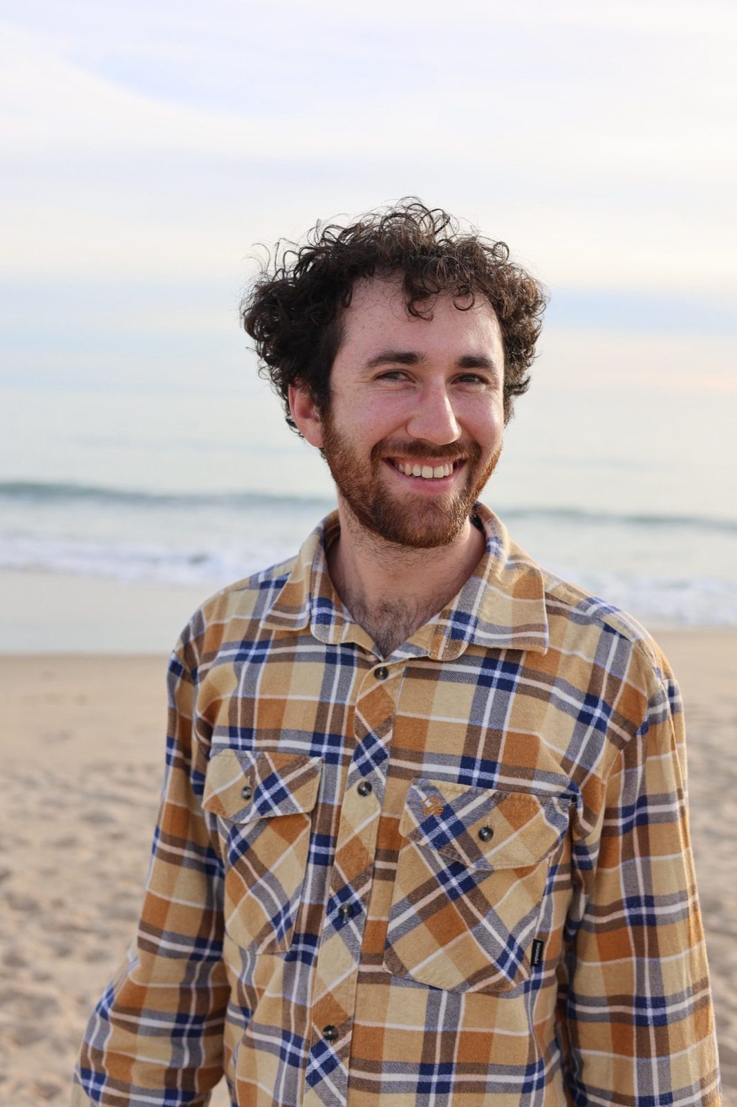 Man with curly hair smiling on the beach